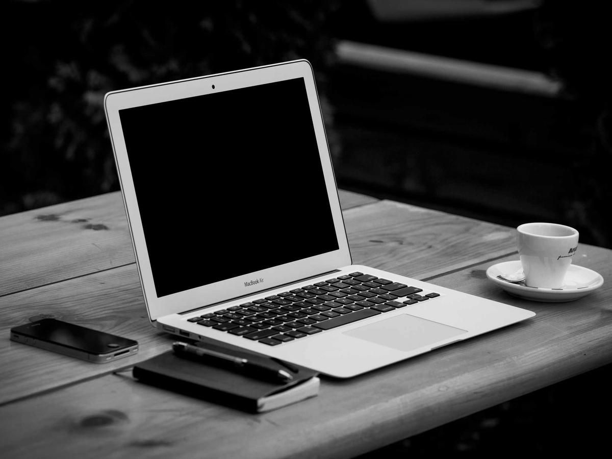 A laptop on a dark wooden table beside a phone and a cup of coffee