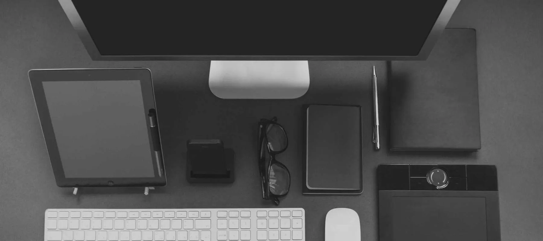 A tidy desk with a monitor, tablet, keyboard and notebook seen from above